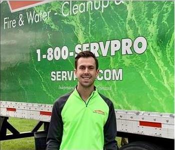 Man with brown hair and beard standing in front of green SERVPRO truck.